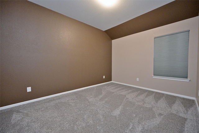 carpeted spare room featuring lofted ceiling and baseboards