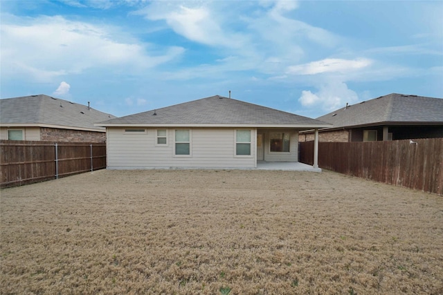 rear view of house featuring a shingled roof, a fenced backyard, a lawn, and a patio area