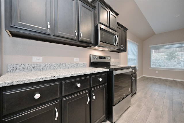 kitchen featuring light wood-style flooring, dark cabinetry, stainless steel appliances, baseboards, and lofted ceiling