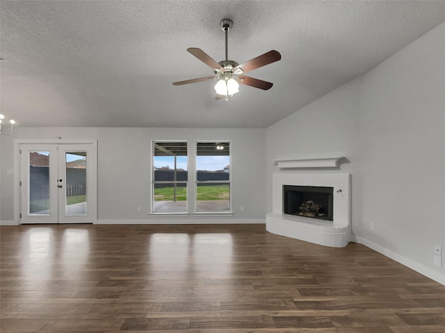 unfurnished living room featuring wood finished floors, baseboards, lofted ceiling, a textured ceiling, and a brick fireplace