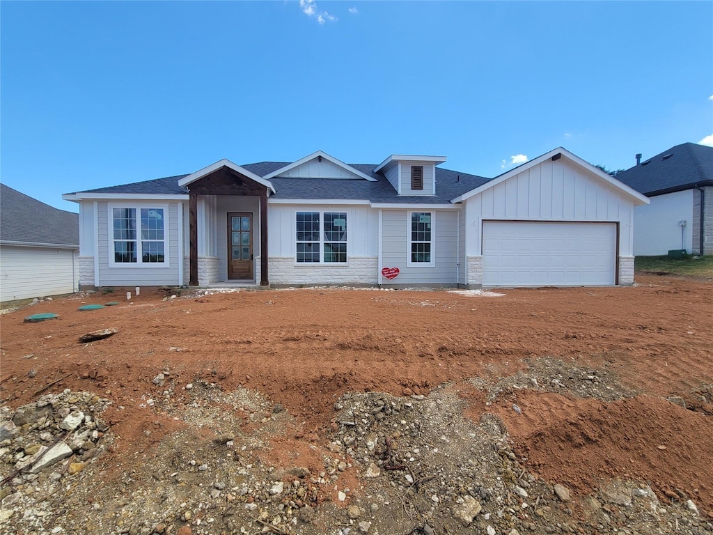 view of front of property with stone siding, an attached garage, board and batten siding, and roof with shingles