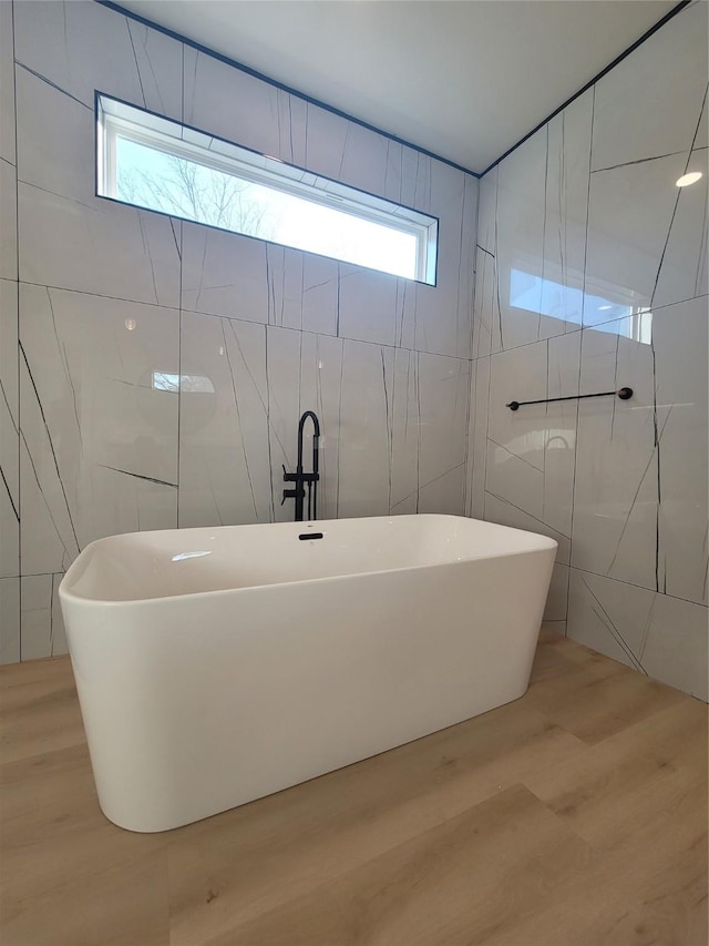 bathroom with a soaking tub, tile walls, and wood finished floors