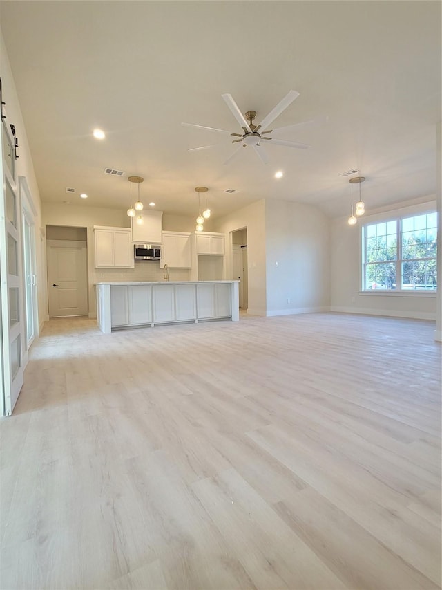 unfurnished living room with visible vents, a barn door, light wood-style flooring, a ceiling fan, and a sink