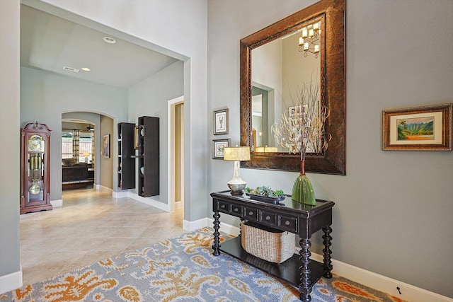 hall featuring baseboards, arched walkways, an inviting chandelier, and tile patterned flooring