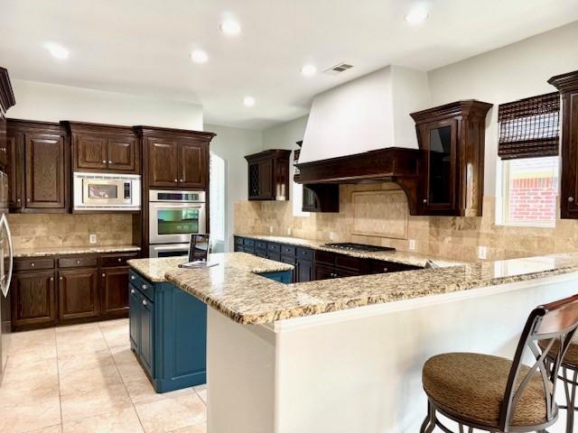 7300 Mitchell Ct, Lantana, TX 76226 - kitchen with stainless steel appliances, backsplash, light stone counters, a kitchen breakfast bar, and light tile patterned floors