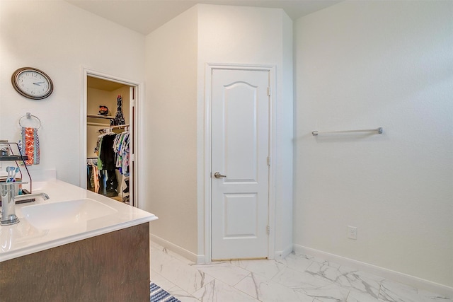 bathroom featuring a spacious closet, marble finish floor, baseboards, and a sink