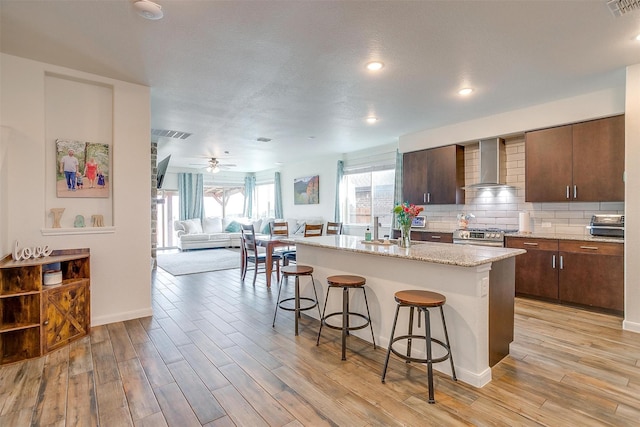 kitchen featuring a kitchen bar, decorative backsplash, light wood finished floors, and wall chimney exhaust hood