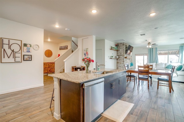 kitchen with light wood-style flooring, a kitchen island with sink, ceiling fan, a sink, and stainless steel dishwasher