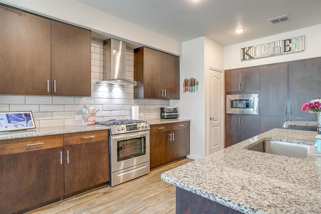 kitchen with visible vents, a sink, appliances with stainless steel finishes, wall chimney range hood, and backsplash