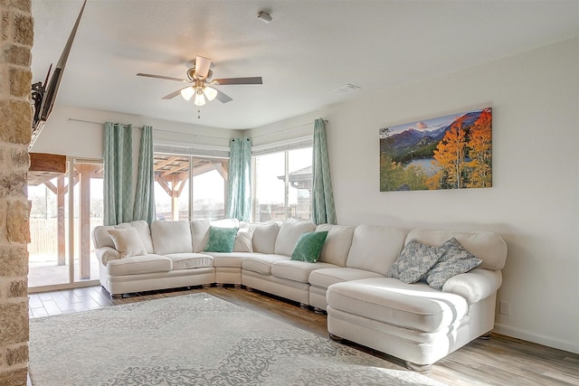 living area with baseboards, wood finished floors, visible vents, and ceiling fan