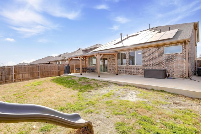 back of house with a patio, a fenced backyard, a lawn, brick siding, and roof mounted solar panels