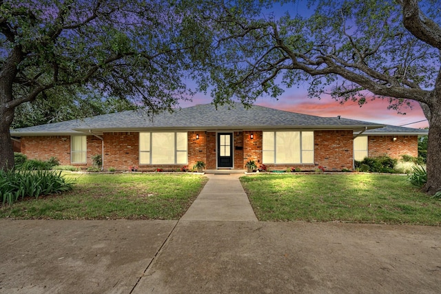 ranch-style home with brick siding, a lawn, and a shingled roof