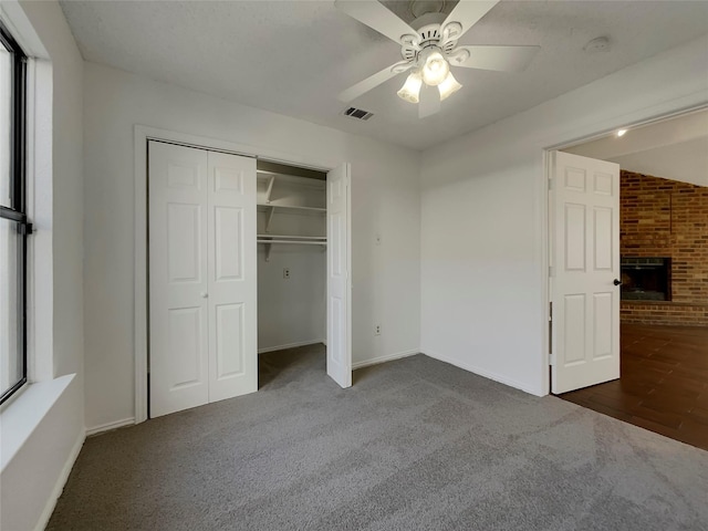 unfurnished bedroom featuring visible vents, a ceiling fan, a closet, carpet floors, and a fireplace