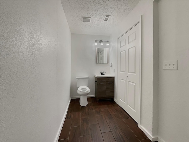 half bath with vanity, a textured ceiling, visible vents, and wood finish floors