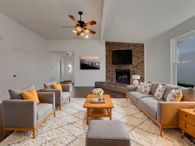 living area with visible vents, ceiling fan, lofted ceiling with beams, a fireplace, and wood finished floors