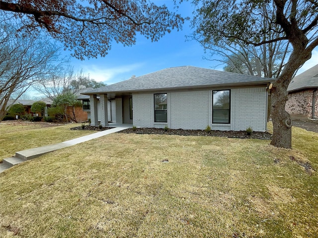 ranch-style house featuring brick siding, a front yard, and roof with shingles