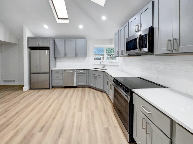 kitchen featuring visible vents, gray cabinets, light wood-style floors, stainless steel appliances, and a sink