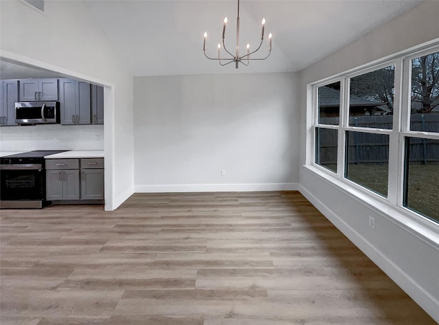 unfurnished dining area with light wood-type flooring, baseboards, an inviting chandelier, and vaulted ceiling