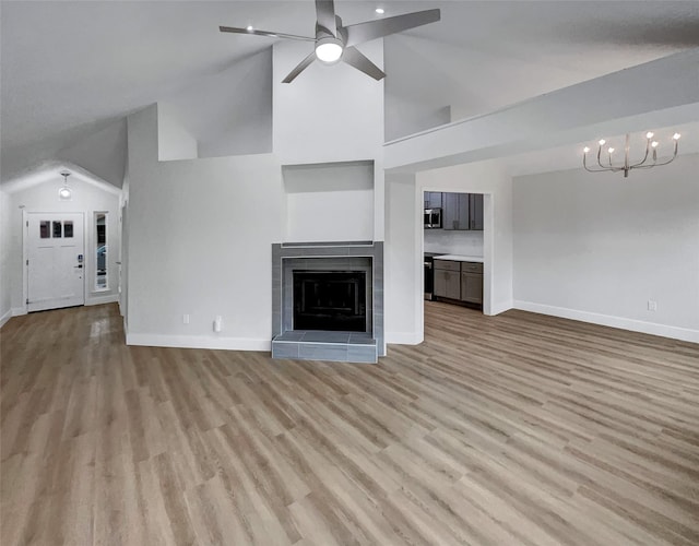 unfurnished living room with light wood-type flooring, high vaulted ceiling, ceiling fan with notable chandelier, a fireplace, and baseboards