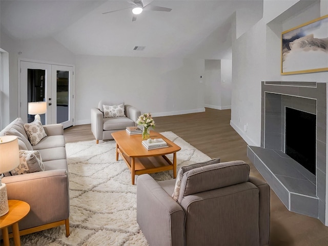 living room with a tiled fireplace, vaulted ceiling, wood finished floors, and french doors