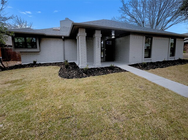 view of front of house with a shingled roof, a front lawn, brick siding, and a chimney