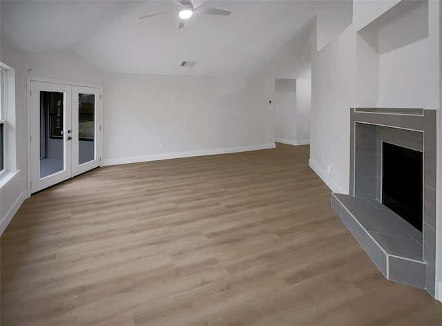 unfurnished living room with light wood-type flooring, a ceiling fan, french doors, a fireplace, and lofted ceiling