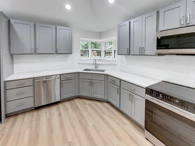 kitchen featuring light wood-type flooring, gray cabinets, a sink, tasteful backsplash, and appliances with stainless steel finishes