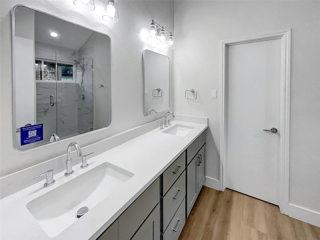 full bathroom featuring a sink, a marble finish shower, wood finished floors, and double vanity