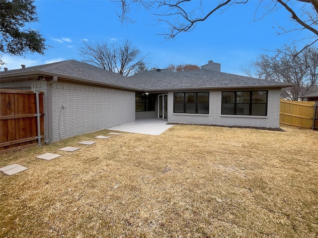 back of house featuring brick siding, fence, a lawn, a chimney, and a patio area