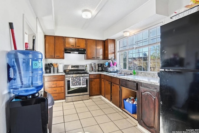 kitchen with light tile patterned floors, freestanding refrigerator, a sink, under cabinet range hood, and stainless steel gas range oven