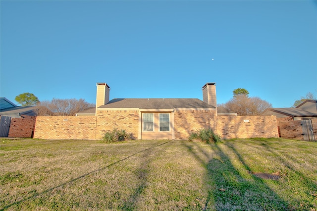 rear view of house featuring brick siding, a lawn, a chimney, and fence