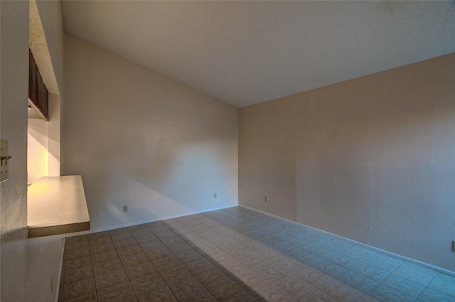 tiled spare room featuring lofted ceiling and baseboards