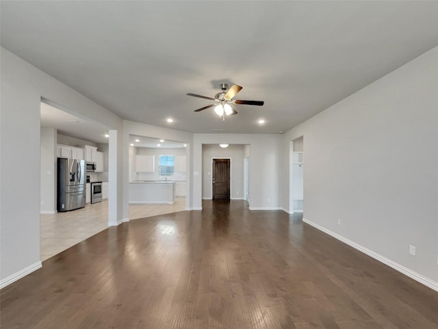 unfurnished living room with ceiling fan, baseboards, and wood finished floors