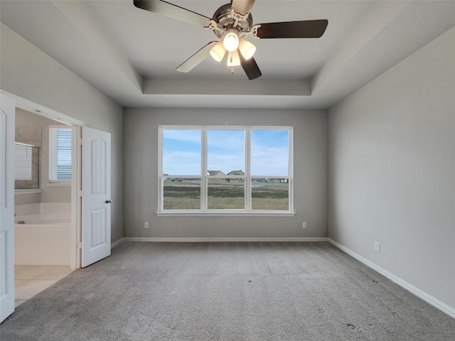 unfurnished bedroom featuring a tray ceiling, carpet flooring, baseboards, and connected bathroom