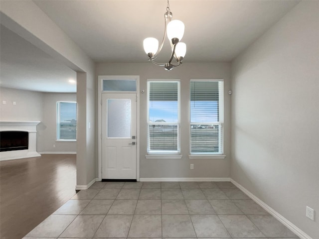 foyer entrance featuring light tile patterned floors, a notable chandelier, a fireplace with raised hearth, and baseboards