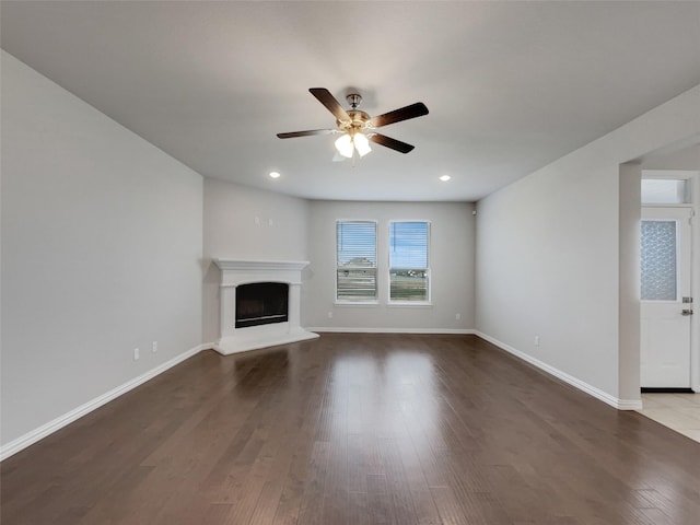 unfurnished living room featuring a fireplace with raised hearth, baseboards, and wood finished floors