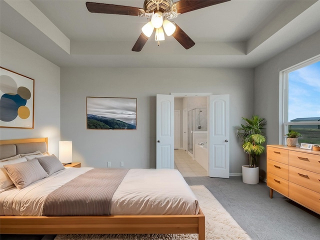 bedroom with light colored carpet, ensuite bath, a raised ceiling, and a ceiling fan