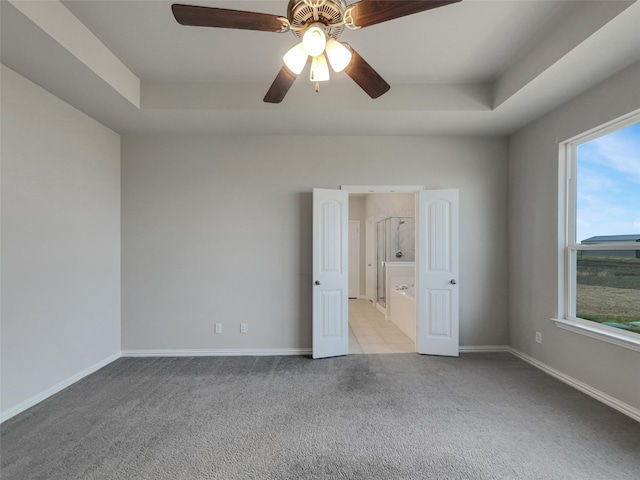 unfurnished room featuring a tray ceiling, light carpet, baseboards, and ceiling fan