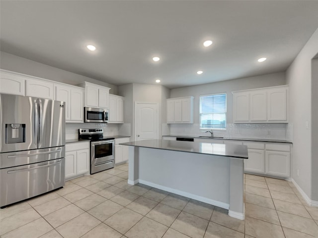 kitchen with light tile patterned floors, a kitchen island, a sink, appliances with stainless steel finishes, and white cabinetry