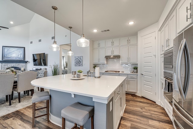 kitchen with tasteful backsplash, under cabinet range hood, a breakfast bar area, appliances with stainless steel finishes, and dark wood-style floors