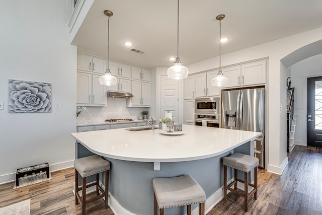 kitchen with a breakfast bar, under cabinet range hood, arched walkways, appliances with stainless steel finishes, and decorative backsplash