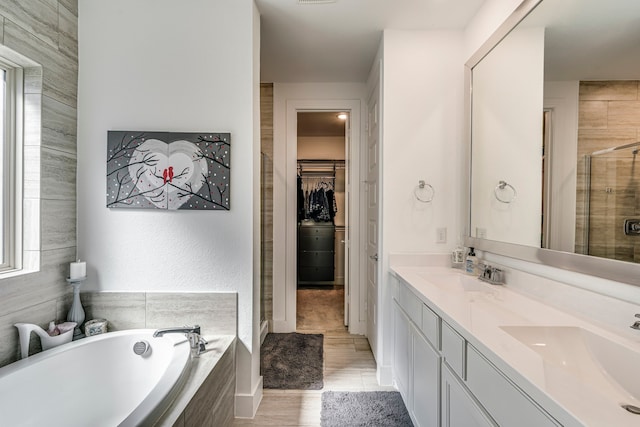 full bath featuring a bath, a shower stall, a walk in closet, and a sink