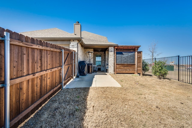 back of property with a patio, a fenced backyard, a shingled roof, brick siding, and a chimney