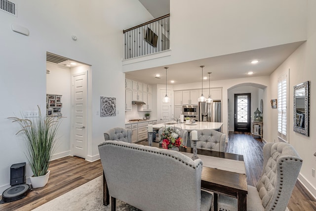 dining space with visible vents, baseboards, arched walkways, dark wood-style flooring, and a towering ceiling