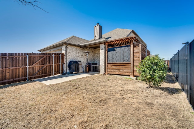 back of house with brick siding, central air condition unit, a chimney, a fenced backyard, and a patio