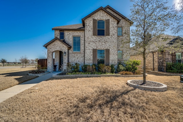 french country style house with brick siding and a front yard