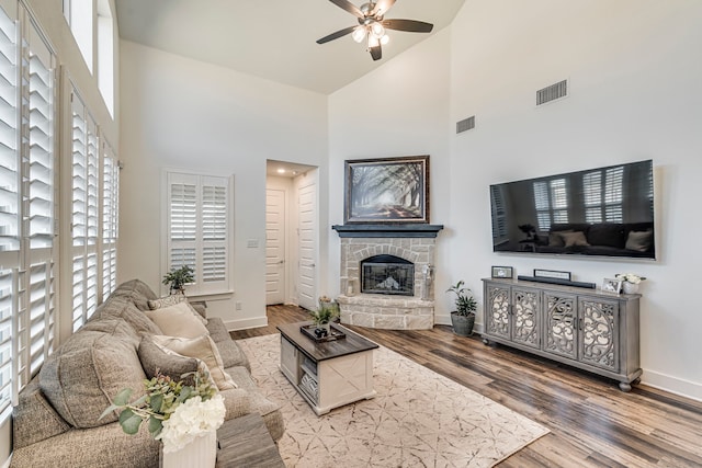 living room featuring visible vents, baseboards, a fireplace, wood finished floors, and a ceiling fan