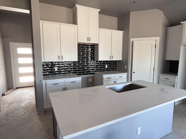 kitchen with backsplash, an island with sink, unfinished concrete floors, and white cabinetry