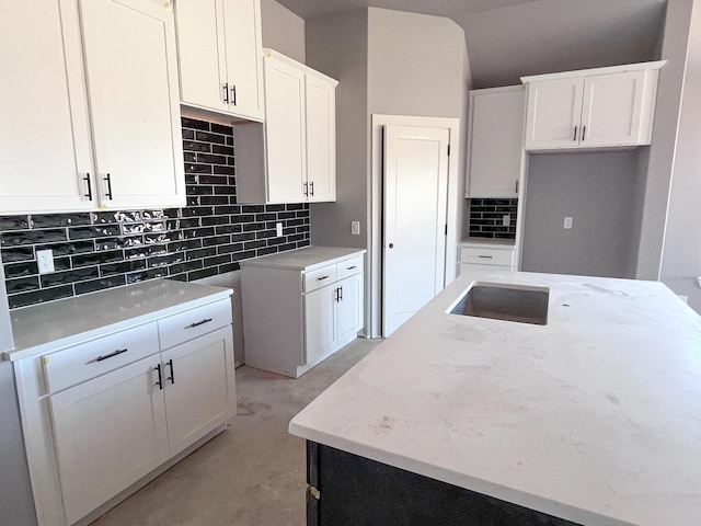 kitchen with white cabinetry, light stone counters, concrete floors, and backsplash