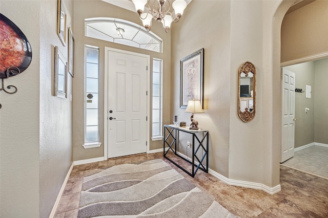 entryway featuring baseboards, a high ceiling, a textured wall, arched walkways, and a notable chandelier